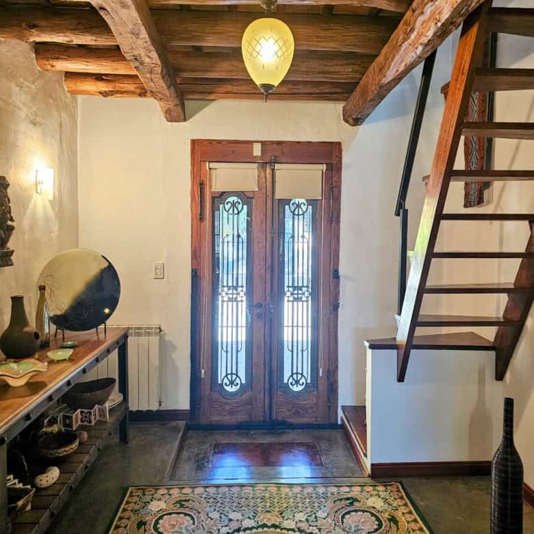 Cozy home entrance featuring wooden beams, a decorative rug, and a wooden staircase. Bright, invitin.
