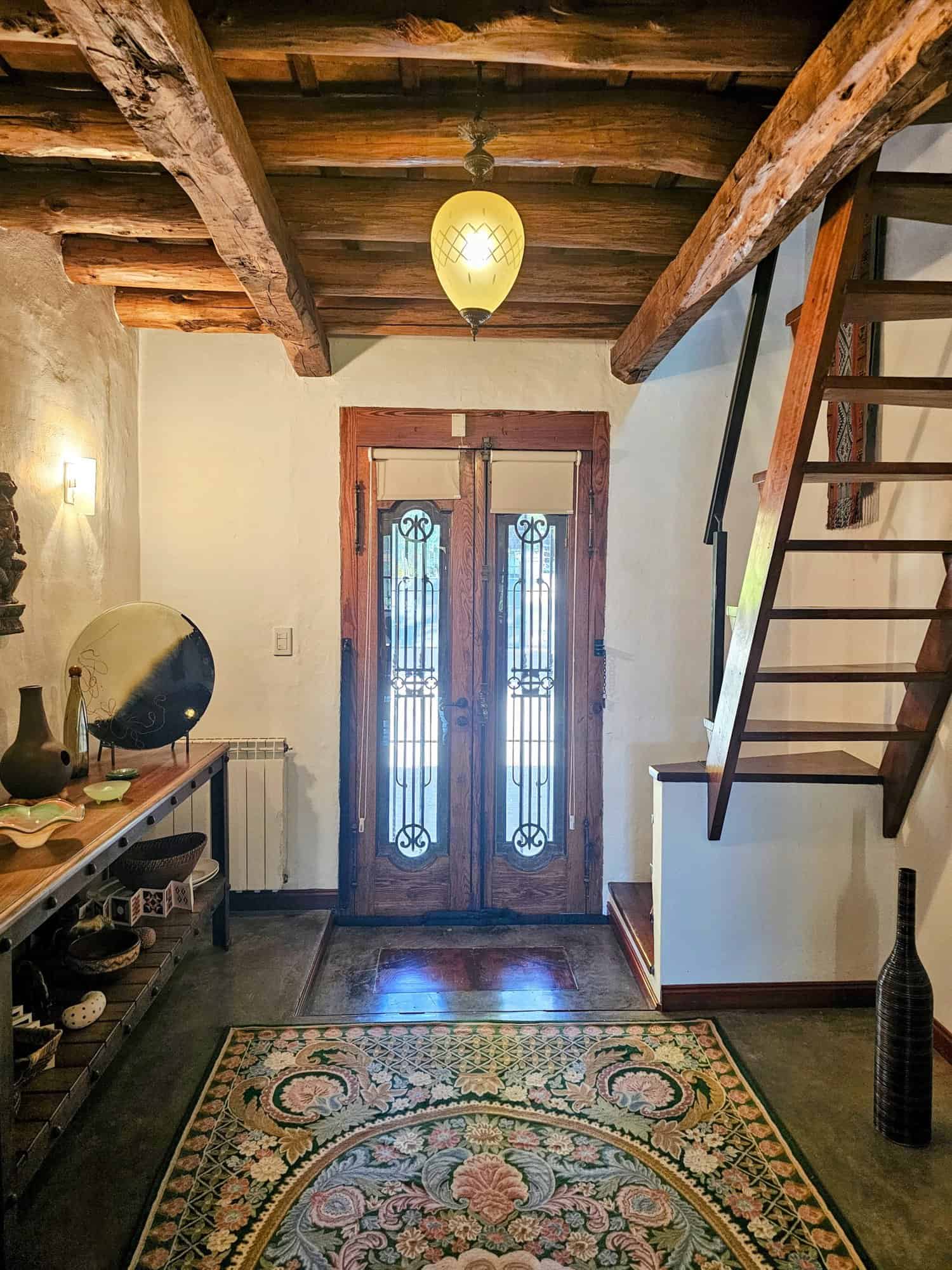 Charming Rustic Interior with Wooden Beams Cozy home entrance featuring wooden beams, a decorative rug, and a wooden staircase. Bright, invitin.