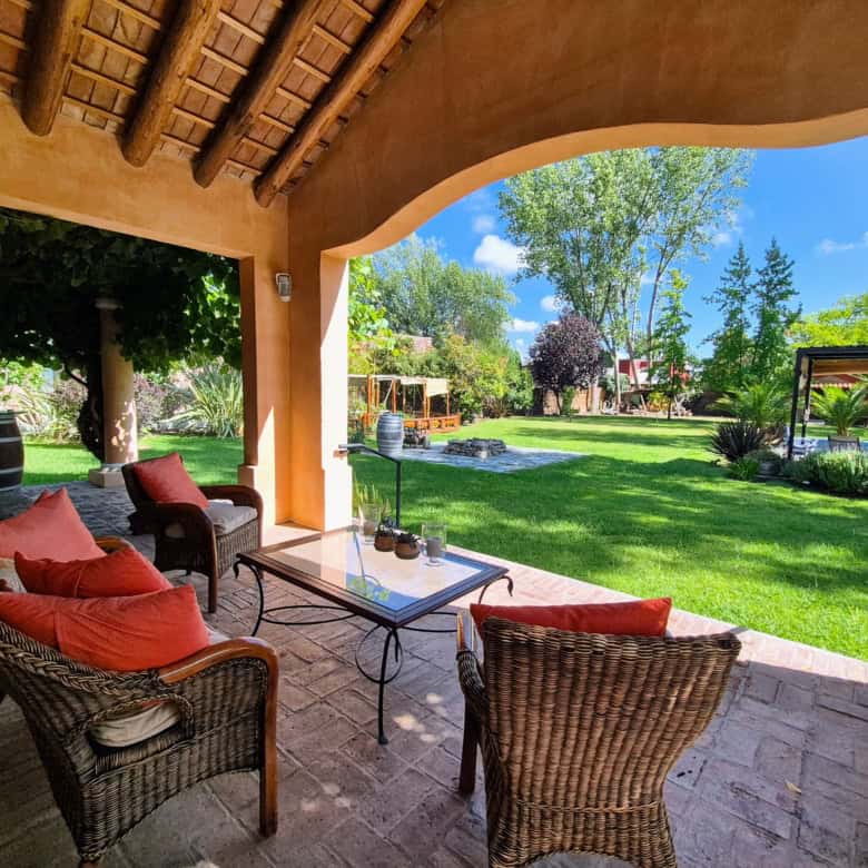 Outdoor patio with wicker furniture and colorful cushions overlooking lush green garden.