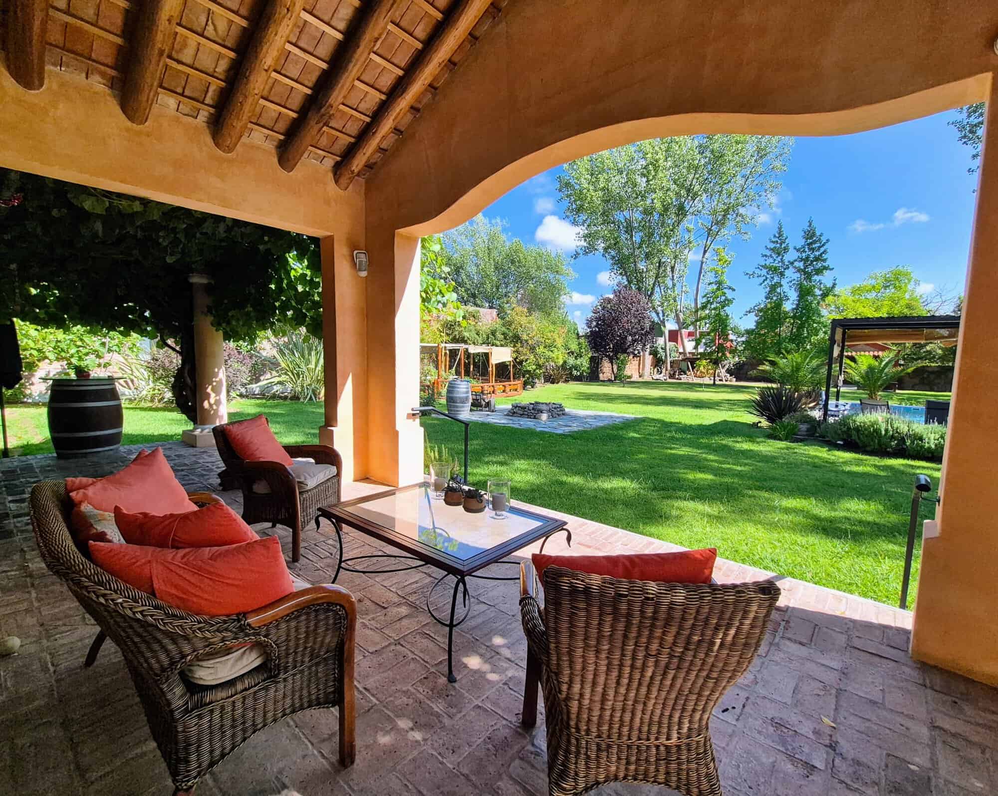 Modern outdoor patio with garden view and seating area Outdoor patio with wicker furniture and colorful cushions overlooking lush green garden.