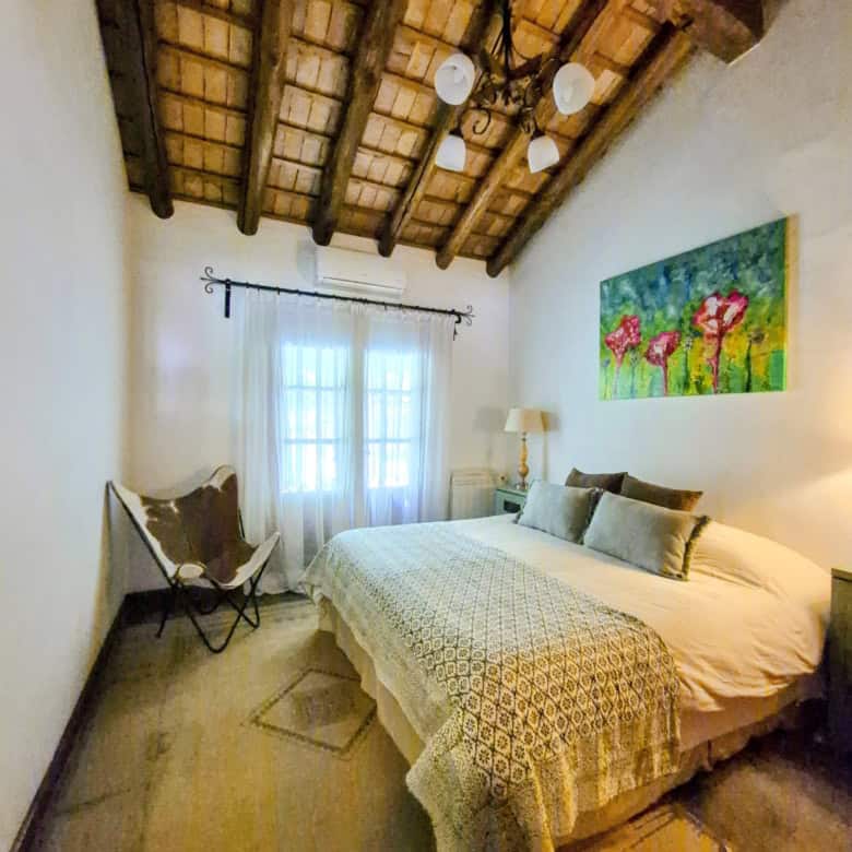 Cozy bedroom featuring wooden ceiling beams, soft lighting, and a comfortable bed with decorative pi.