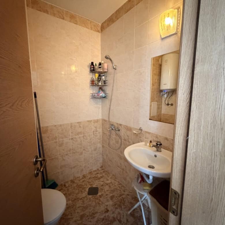 Bathroom with shower, sink, and storage shelves in a top floor apartment.