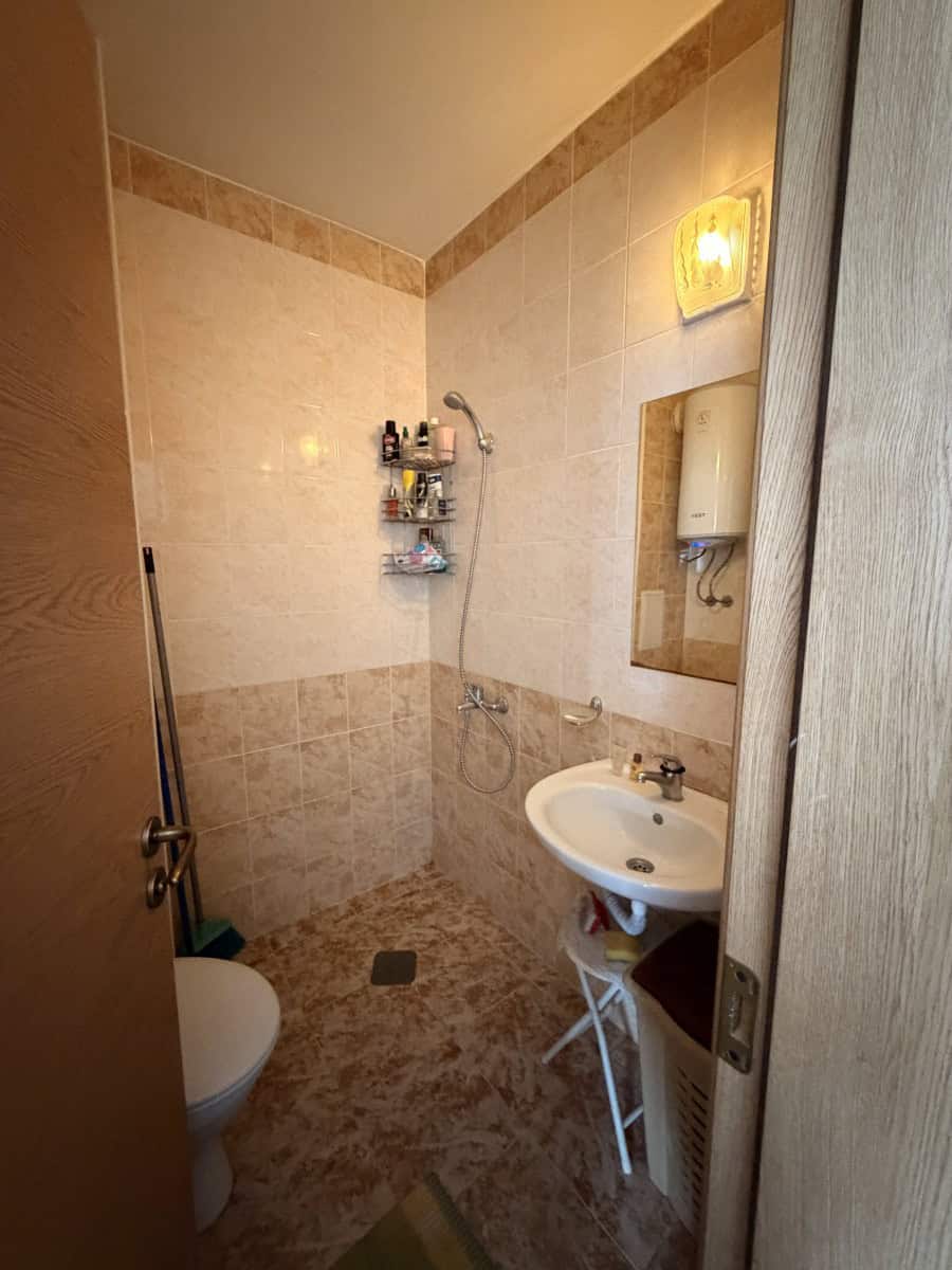 Bathroom with shower, sink, and storage shelves in a top floor apartment.