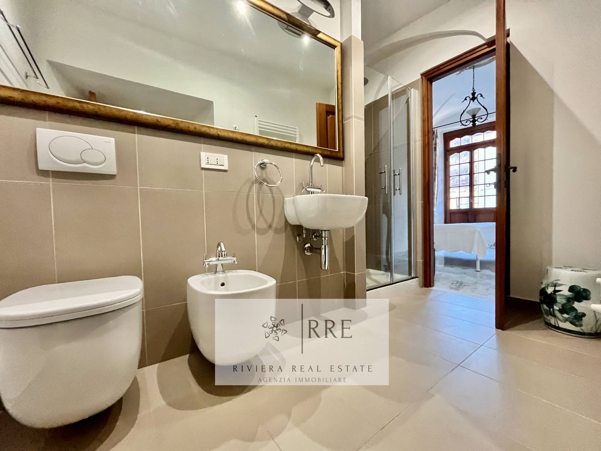Bright modern bathroom featuring a toilet, bidet, and sink with a large mirror and natural light.