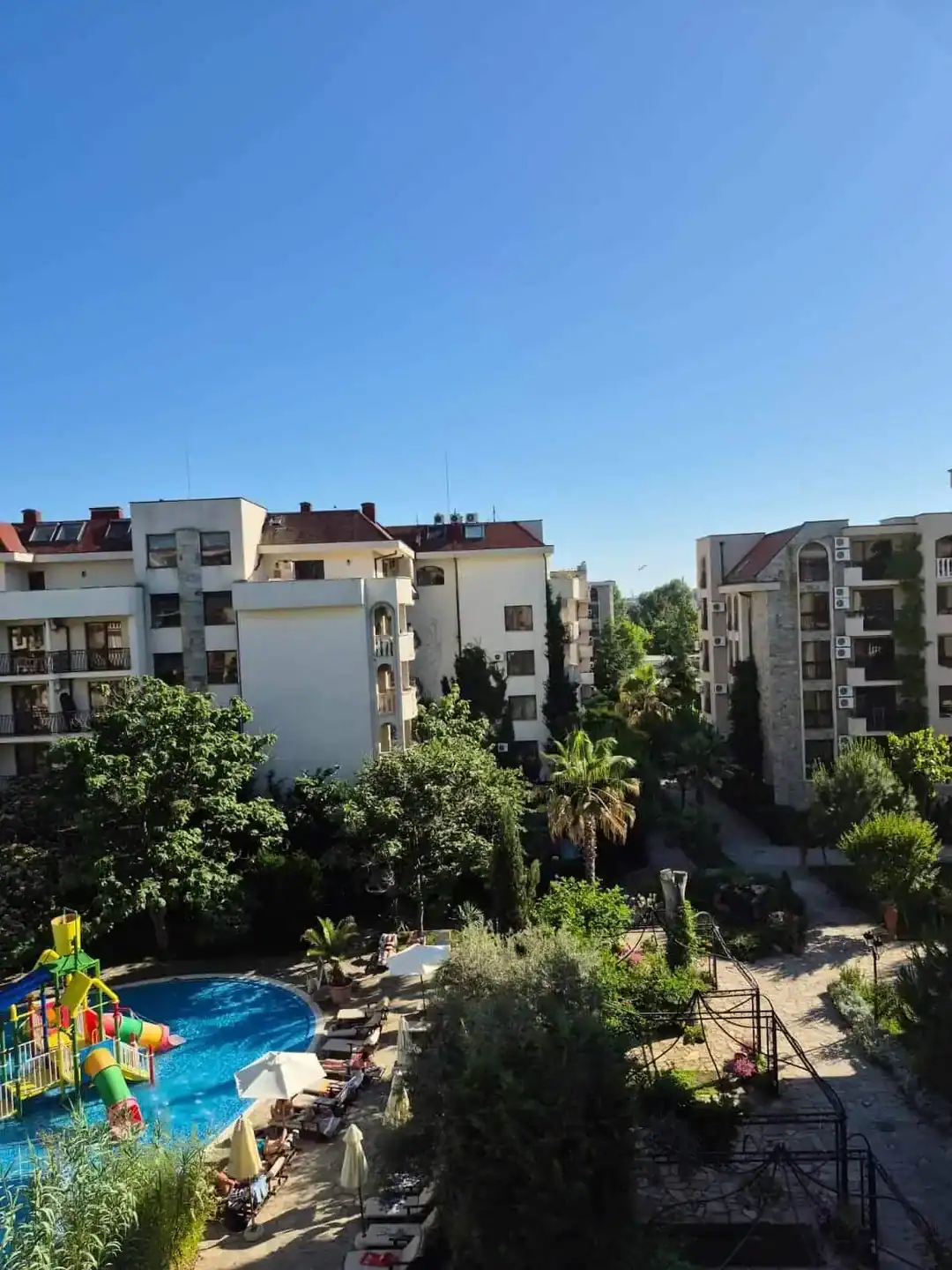 Contemporary residential buildings surrounded by trees and a vibrant pool area.