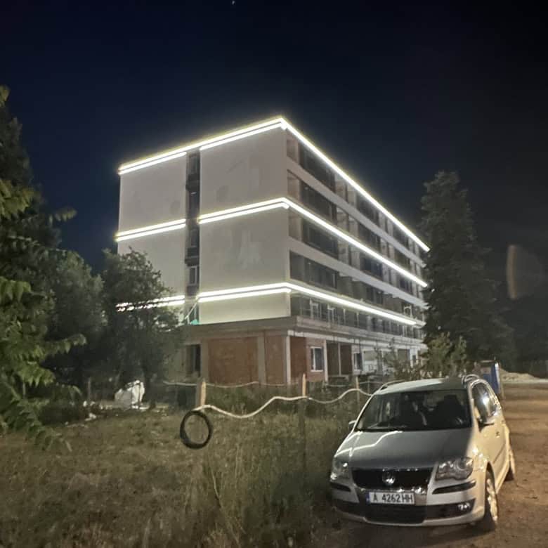 Brightly lit luxury apartment complex with sleek design and pool in Sunny Beach at night.