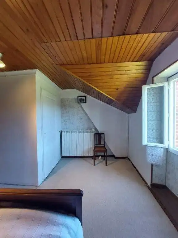 Cozy attic bedroom with wooden ceiling, white walls, and a window overlooking the countryside in Mad.
