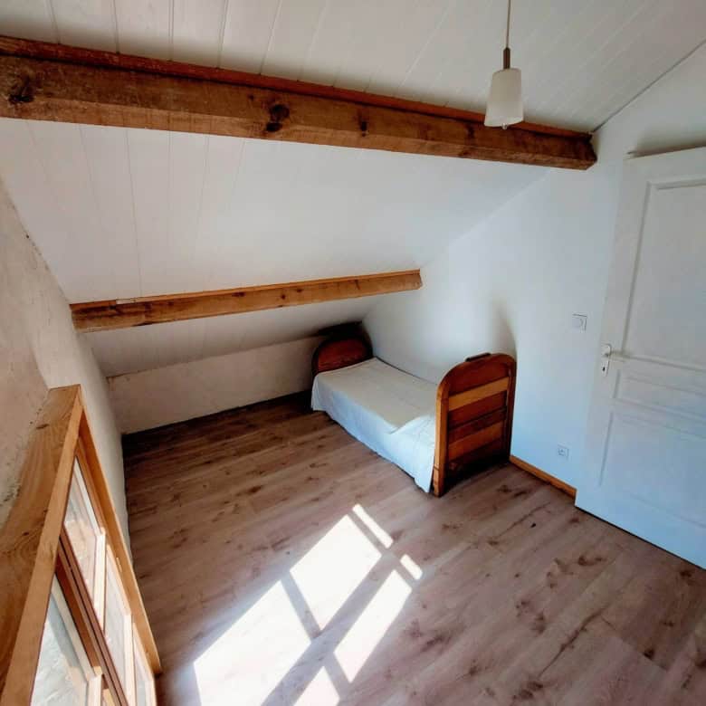 Cozy bedroom with sloped ceiling and wooden beams in a picturesque Madiran village farmhouse.