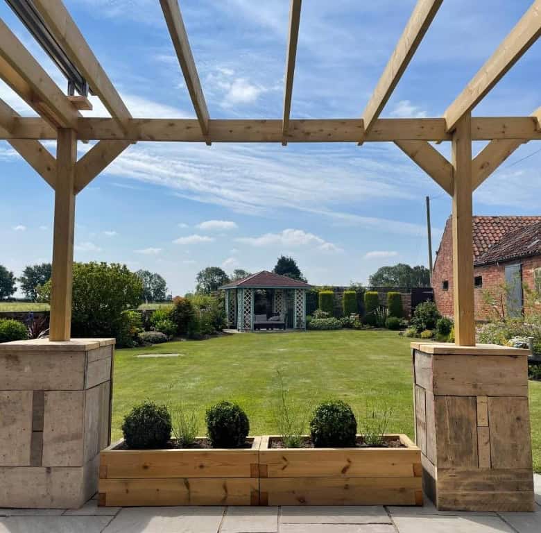 Stylish outdoor pergola with wooden beams and stone supports in a lush garden setting.