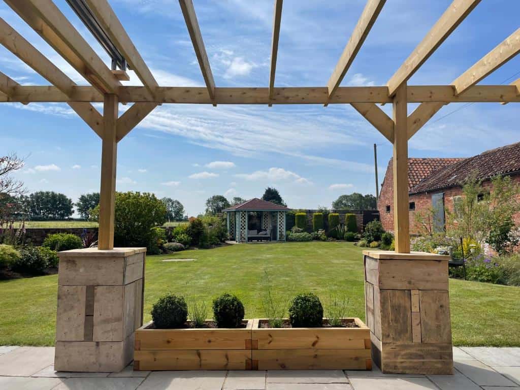 Modern garden pergola structure for outdoor living Stylish outdoor pergola with wooden beams and stone supports in a lush garden setting.