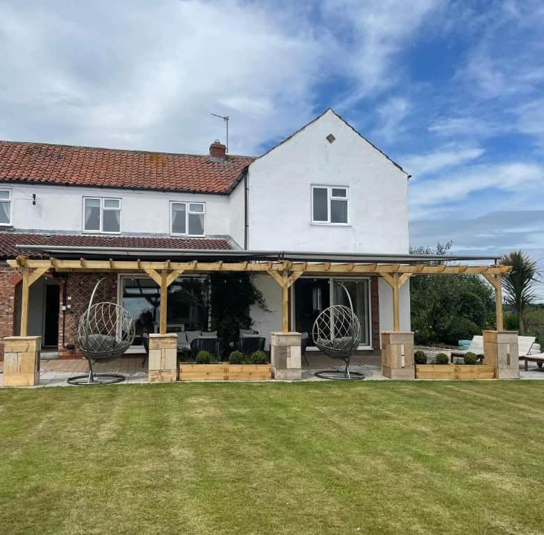 Country house with outdoor patio, garden, and lounge chairs under a wooden pergola.