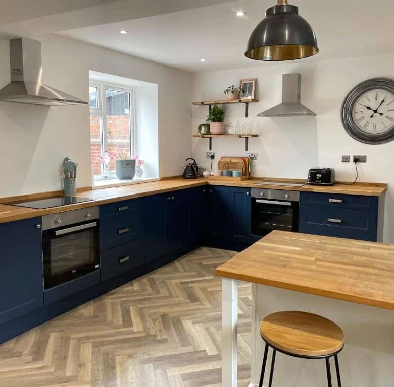 Modern kitchen with navy blue cabinets, wooden countertops, and stainless steel appliances.