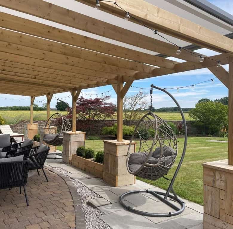 Outdoor patio with hanging egg chairs, seating area, and lush garden backdrop.