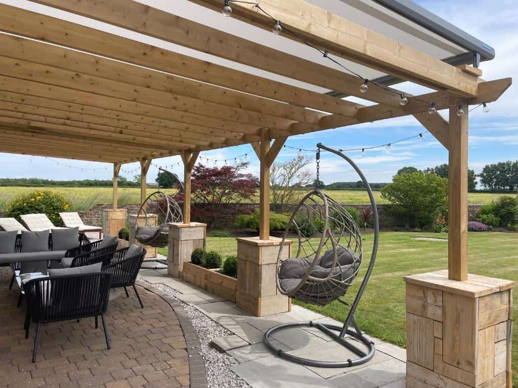 Modern outdoor patio with hanging egg chairs and garden view Outdoor patio with hanging egg chairs, seating area, and lush garden backdrop.
