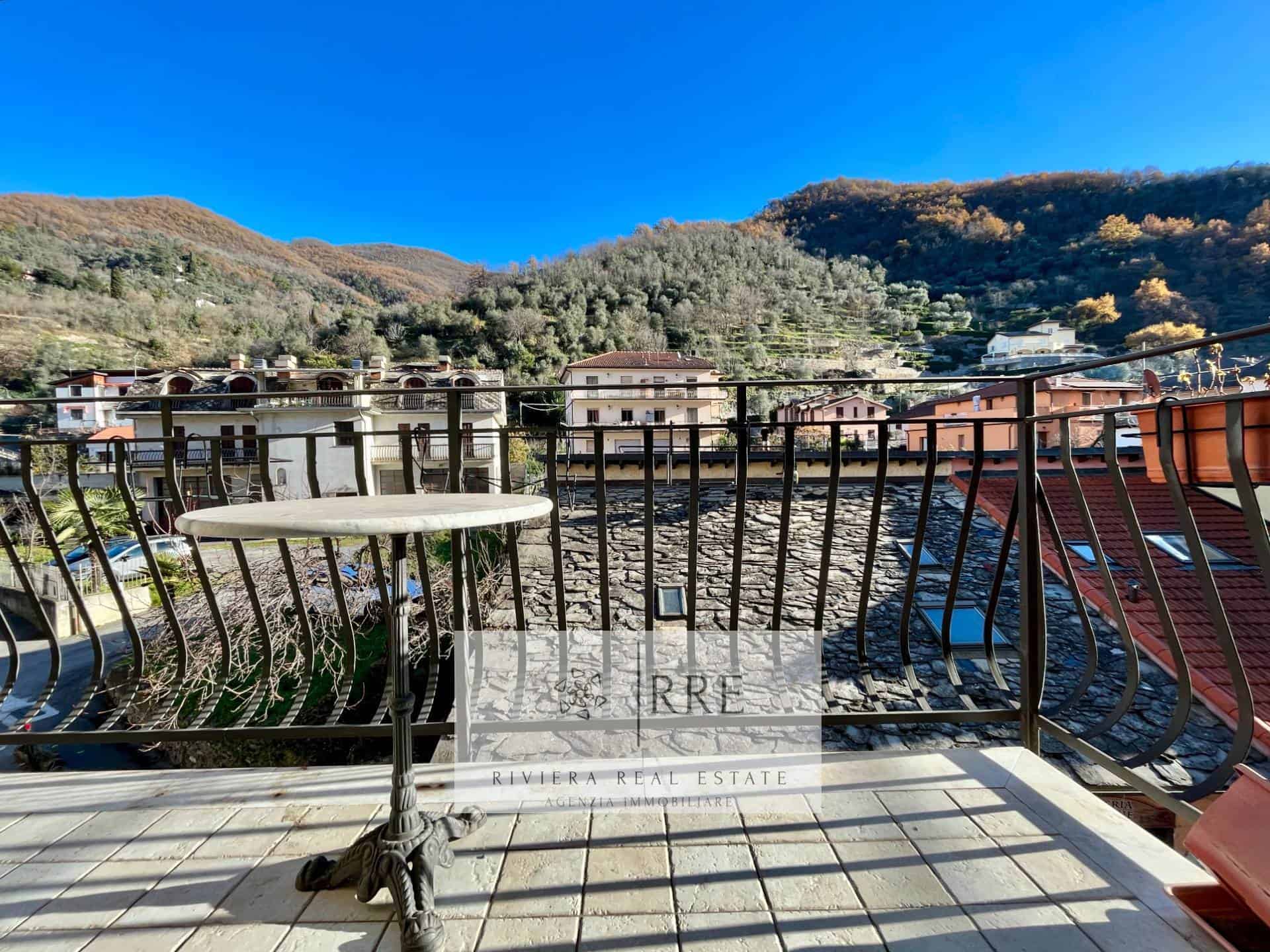 Balcony with metal railing overlooking a scenic mountain landscape and neighboring houses under a cl.