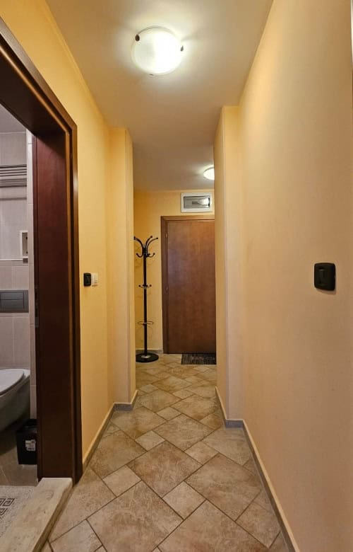 Interior view of a hallway in a modern apartment with warm yellow walls and tiled flooring.