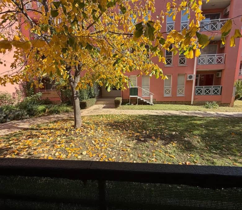 Bright autumn scene outside a pink apartment building with yellow leaves and a sunny day.