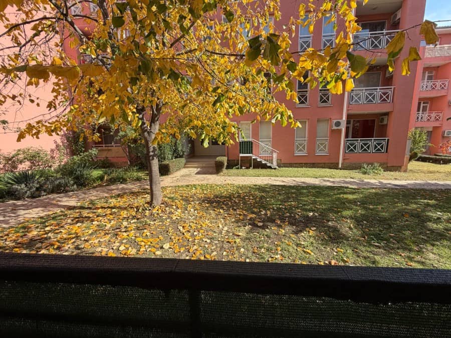 Bright autumn scene outside a pink apartment building with yellow leaves and a sunny day.