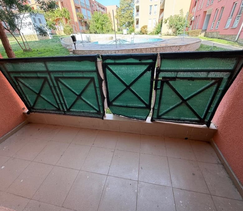 Balcony overlooking a swimming pool and lush garden in a sunny apartment complex.