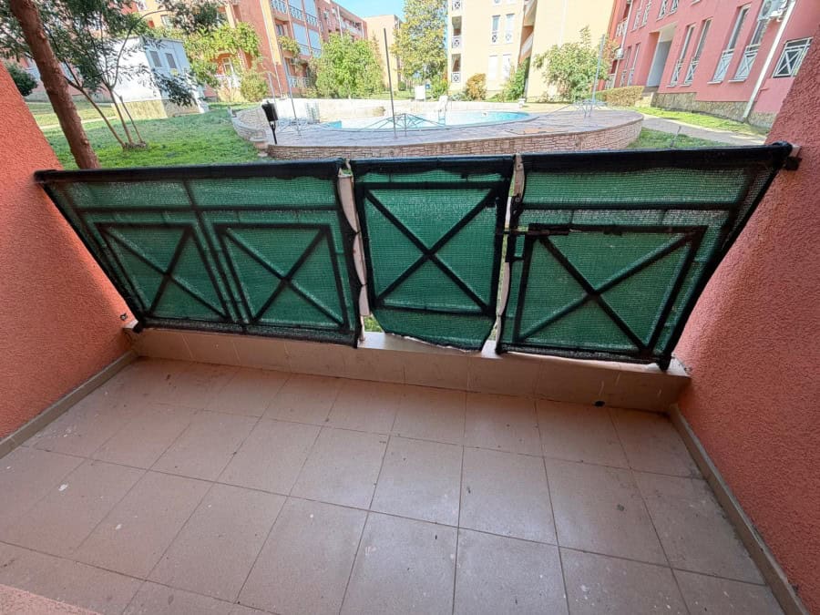 Balcony overlooking a swimming pool and lush garden in a sunny apartment complex.