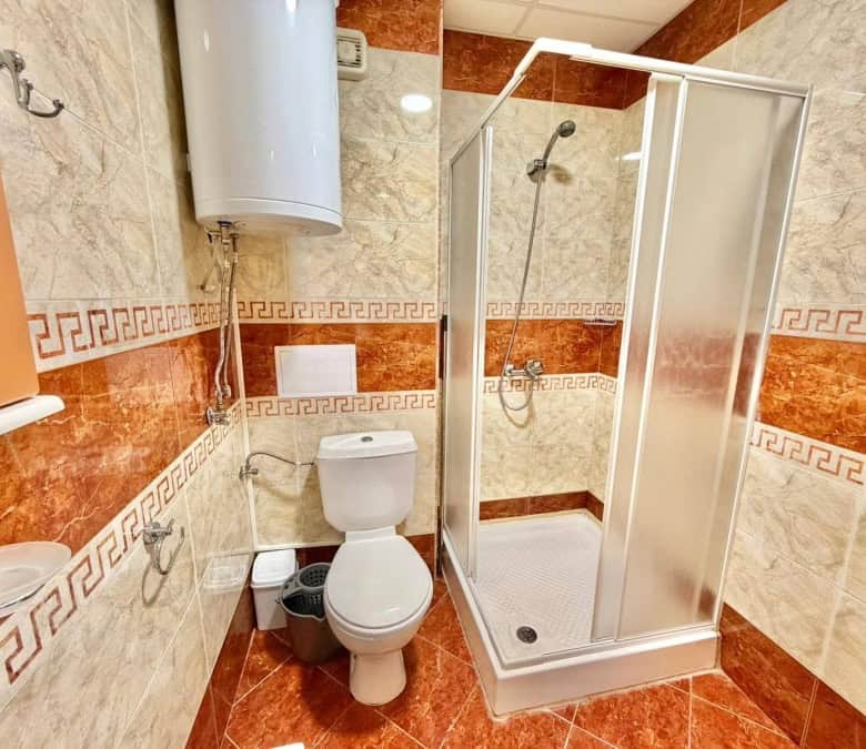 Bright bathroom with shower cabin, toilet, and water heater in a 2-bedroom apartment.