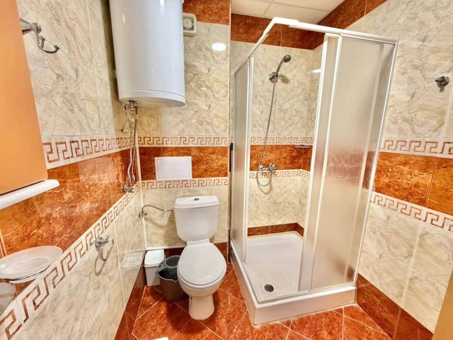Bright bathroom with shower cabin, toilet, and water heater in a 2-bedroom apartment.