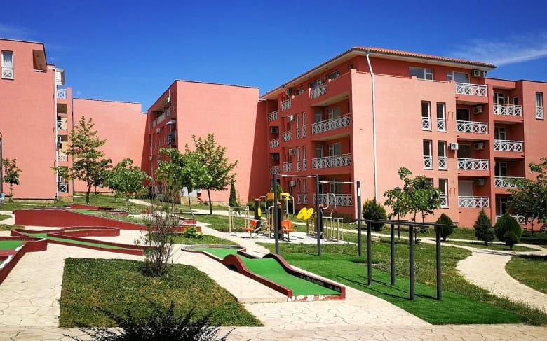 Bright pink apartment buildings with balconies and green outdoor space in Sunny Beach.