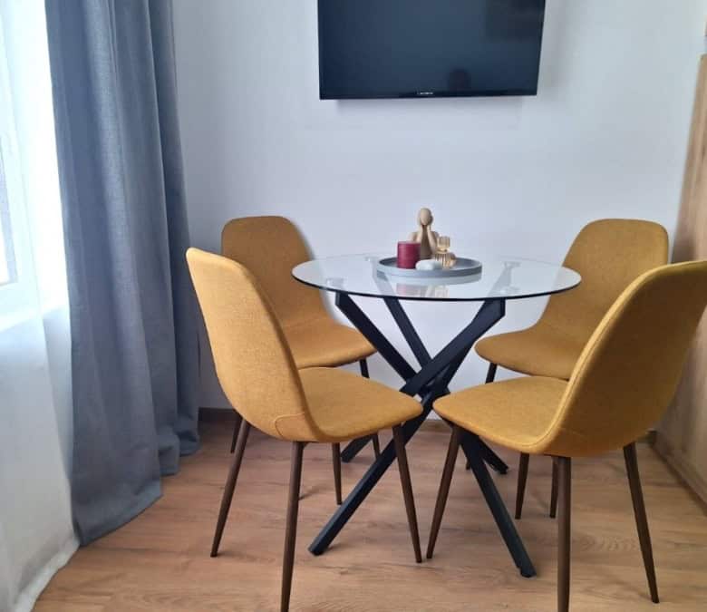 Bright dining area with four mustard-colored chairs and glass table in Sunny Day 3 apartment.