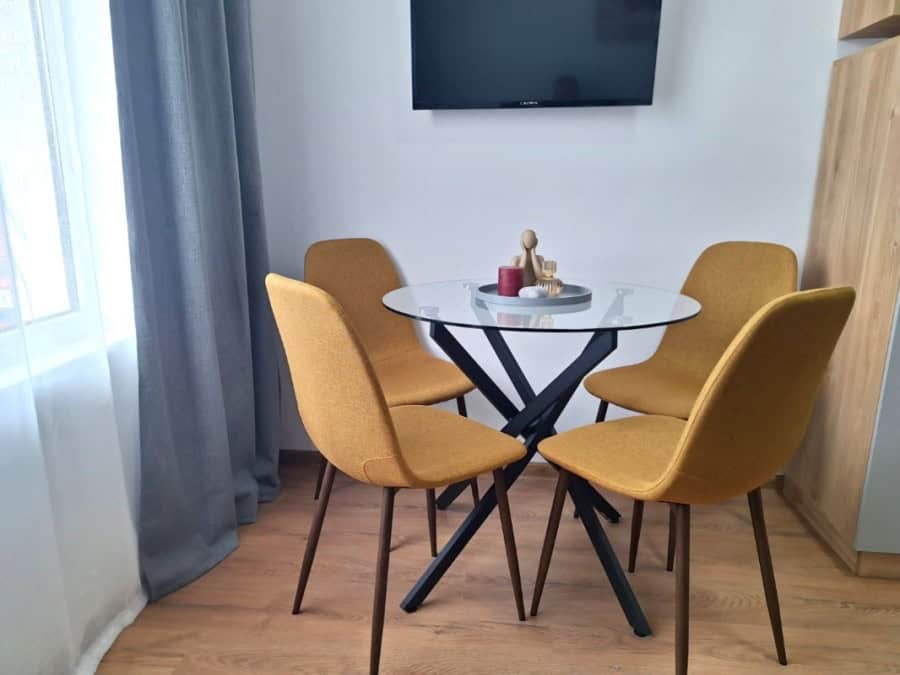 Bright dining area with four mustard-colored chairs and glass table in Sunny Day 3 apartment.