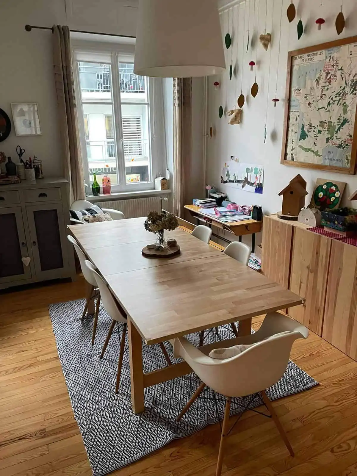 Bright dining area with wooden table, white chairs, and colorful wall decorations.