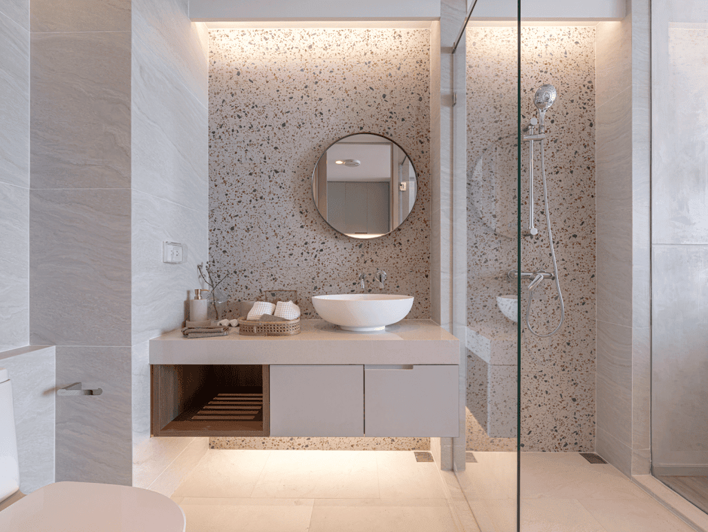 Elegant bathroom featuring a round mirror, vessel sink, and glass-enclosed shower.