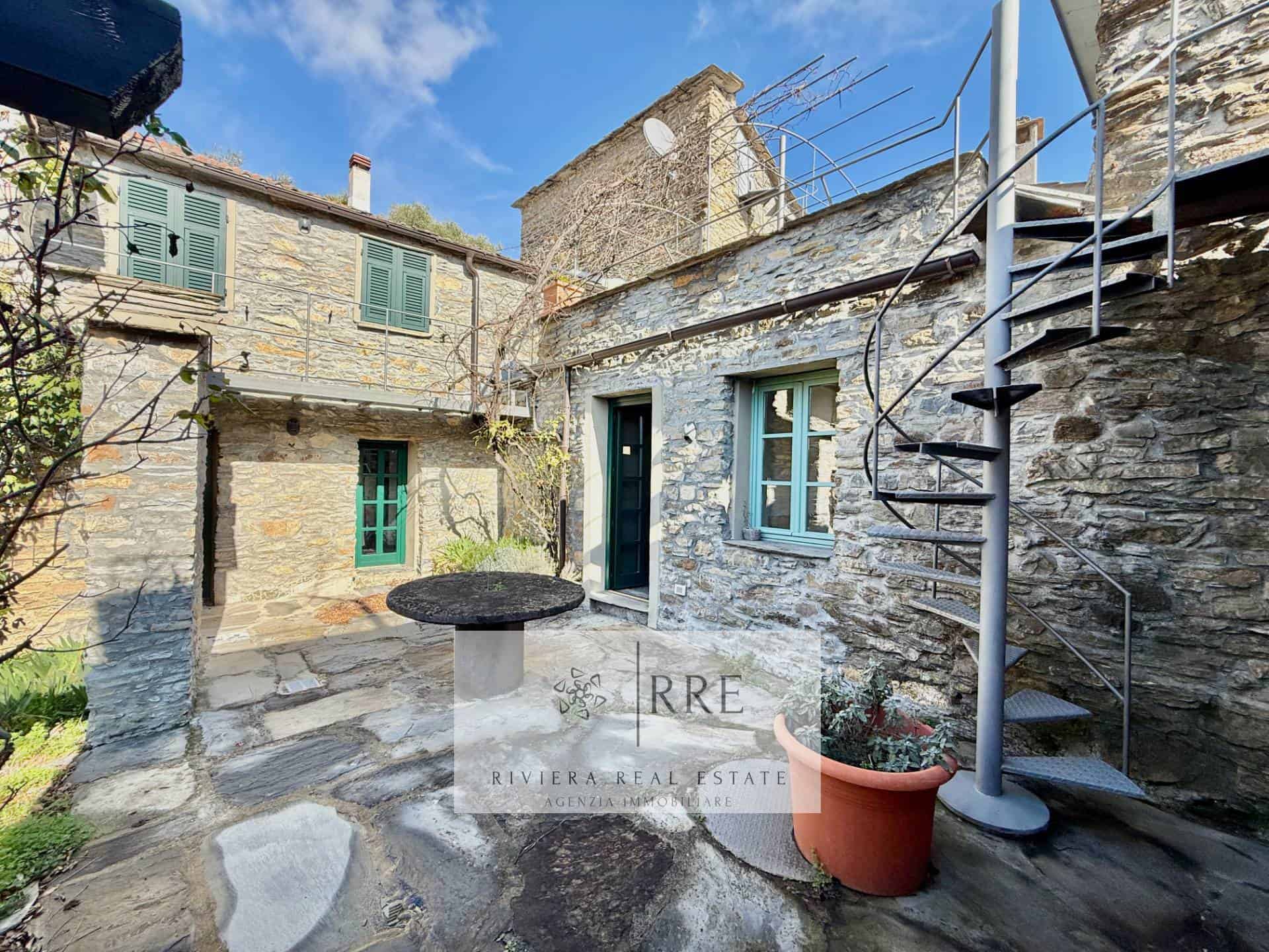 Cozy courtyard with stone walls, outdoor seating, and spiral staircase in a historic village setting.