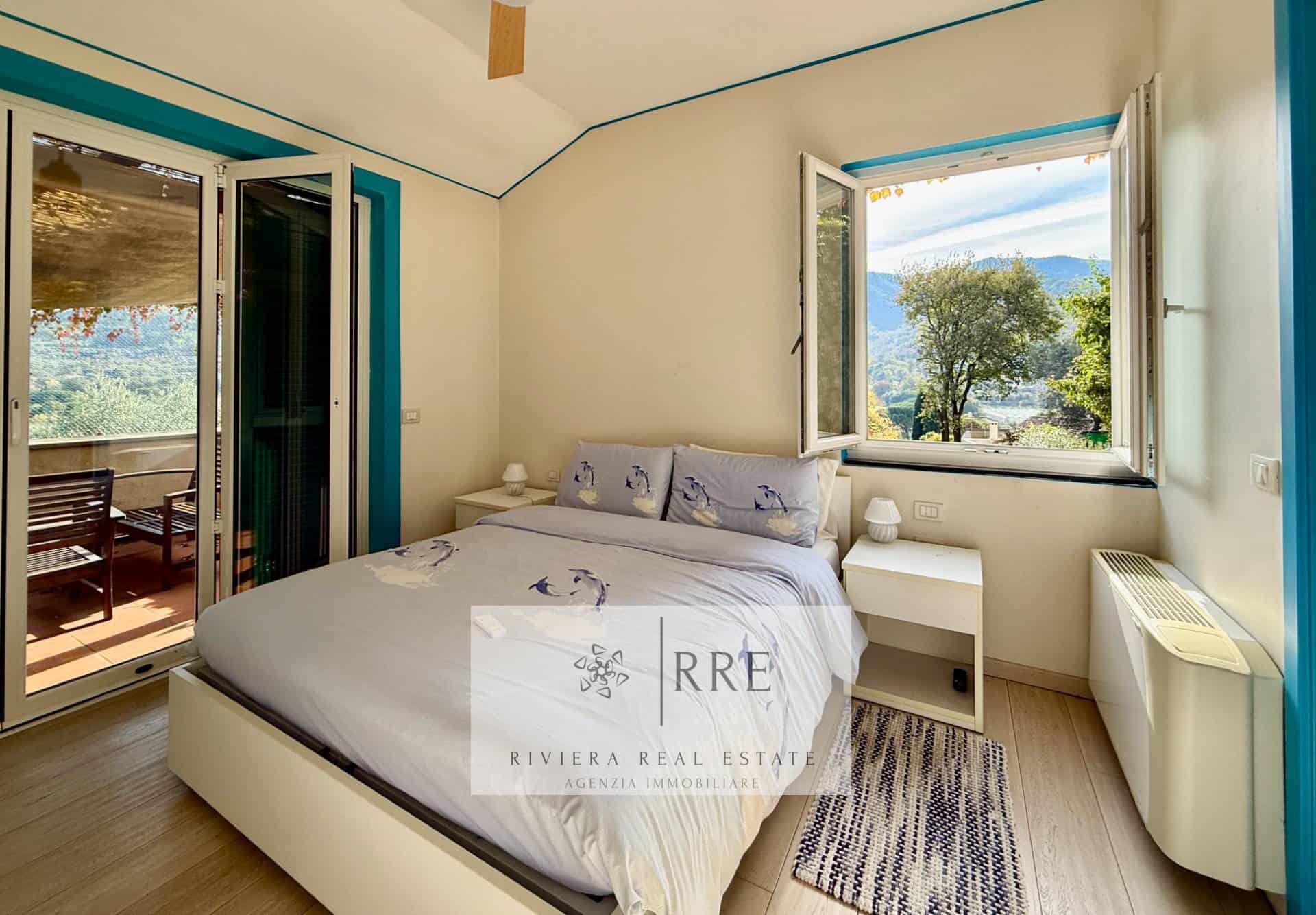 Beachside bedroom with open window and scenic view of trees and mountains.