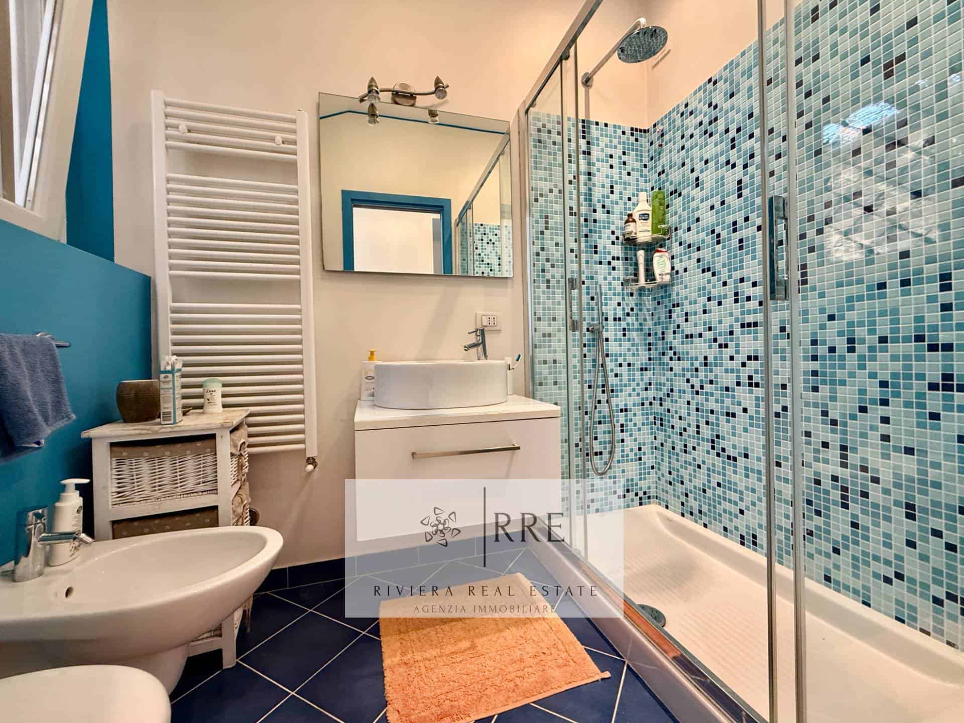 Bathroom with walk-in shower featuring blue mosaic tiles and modern fixtures.