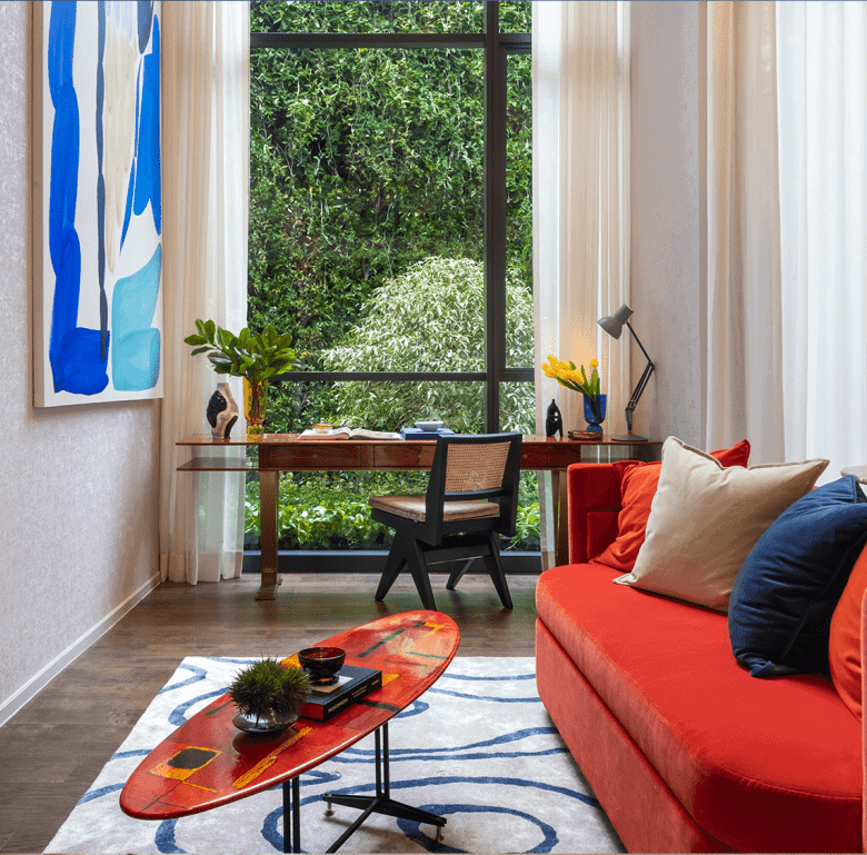 Bright living room with colorful sofa, decorative pillows, and a view of lush greenery outside.