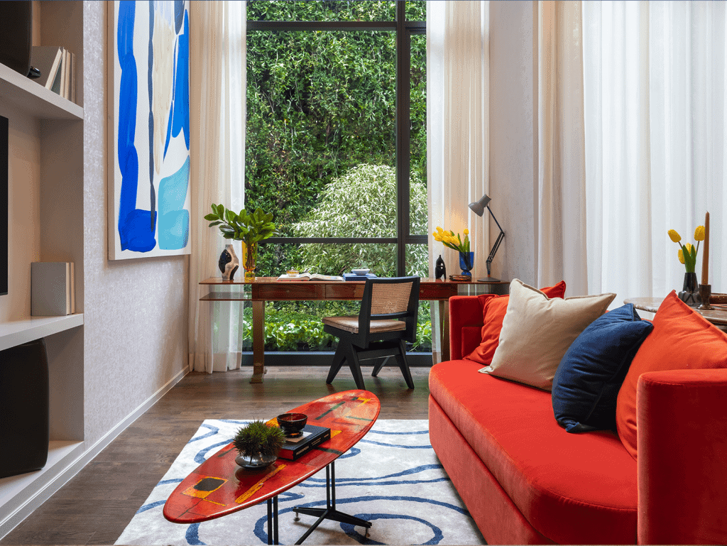 Bright living room with colorful sofa, decorative pillows, and a view of lush greenery outside.