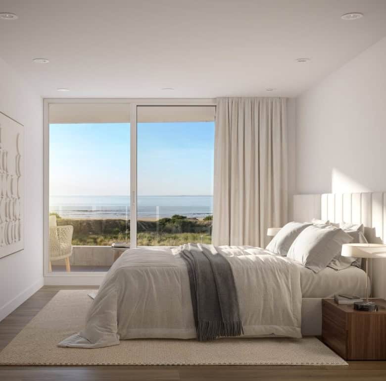 Ocean view bedroom with large window, white decor, and cozy bedding in Casa Rambla.