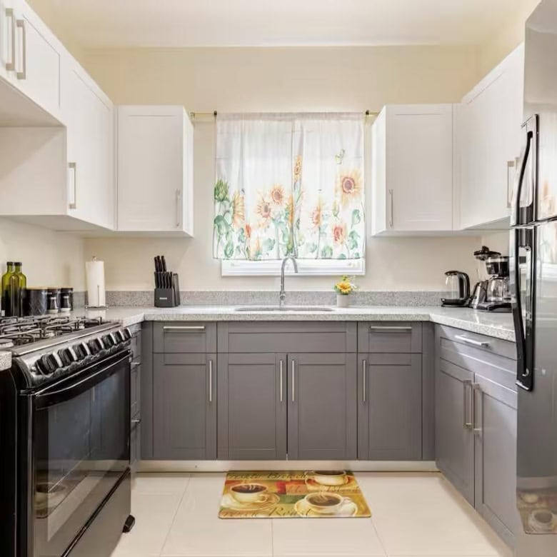 Bright kitchen with white and gray cabinetry, stainless steel appliances, and a floral window curtai.