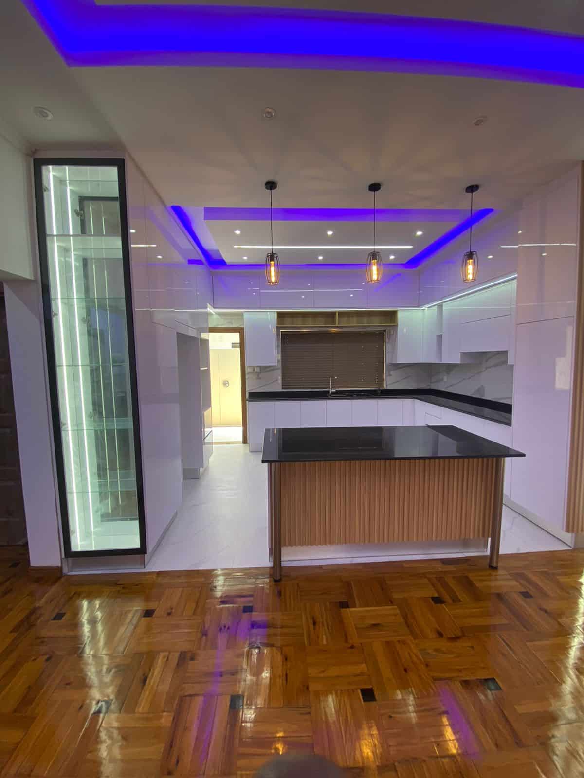 Modern kitchen with sleek white cabinets and blue LED ceiling lights.