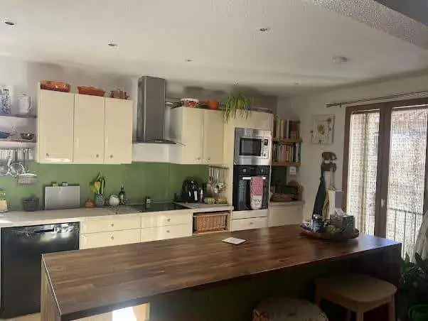 Modern kitchen with white cabinets, green backsplash, and wooden island in a renovated village house.