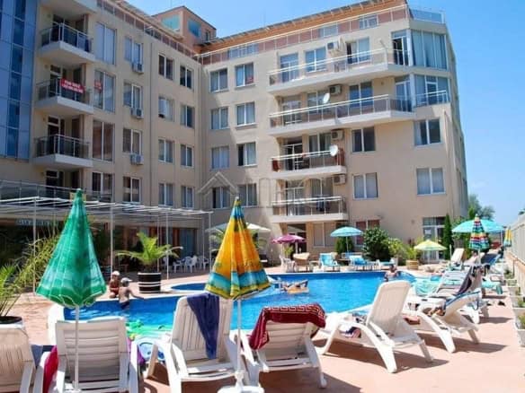 Poolside view of Balkan Breeze 1-bedroom apartment with sun loungers and umbrellas in Sunny Beach.