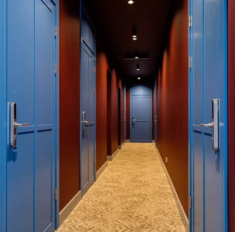 Corridor with blue doors in a hotel, featuring warm lighting and a carpeted floor.