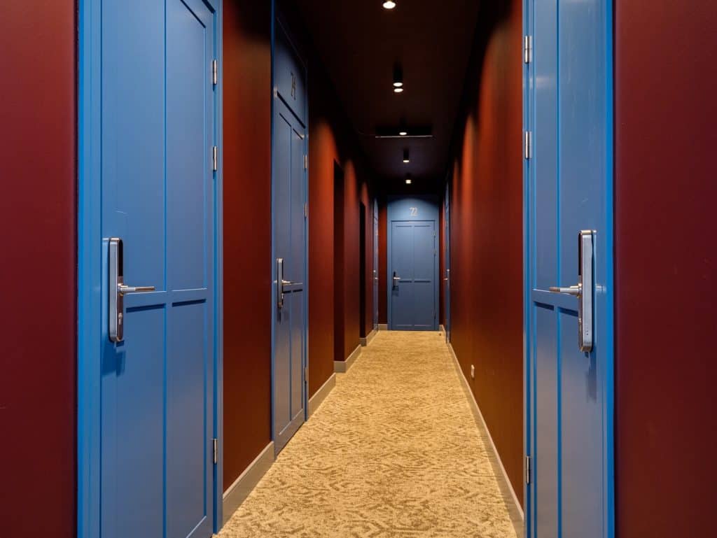 Corridor with blue doors in a hotel, featuring warm lighting and a carpeted floor.