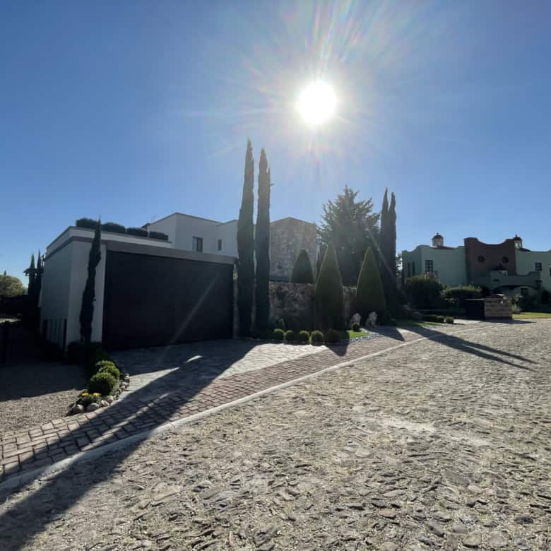 Modern villa with tall cypress trees and bright sun in the sky.