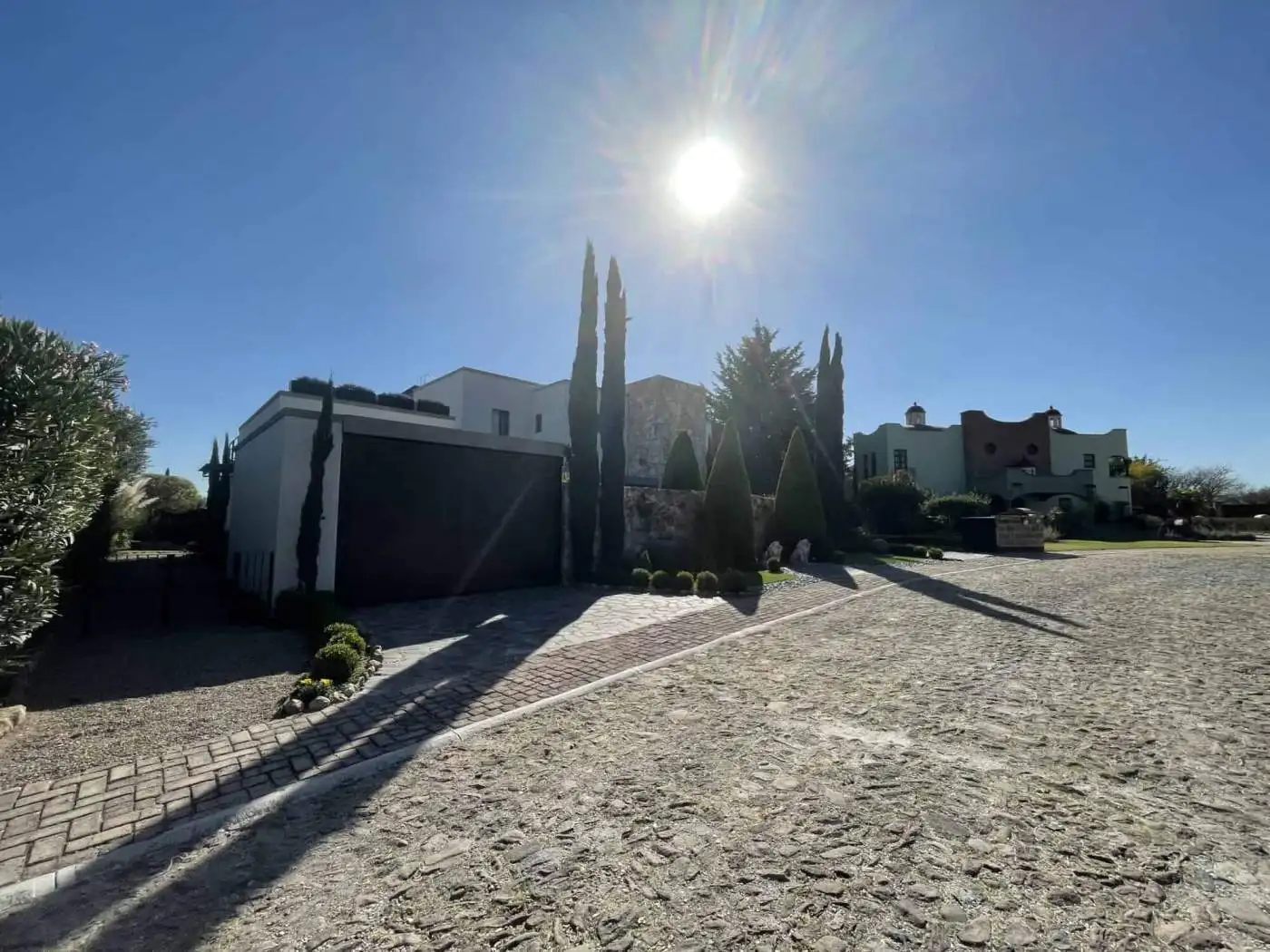 Modern villa with tall cypress trees and bright sun in the sky.