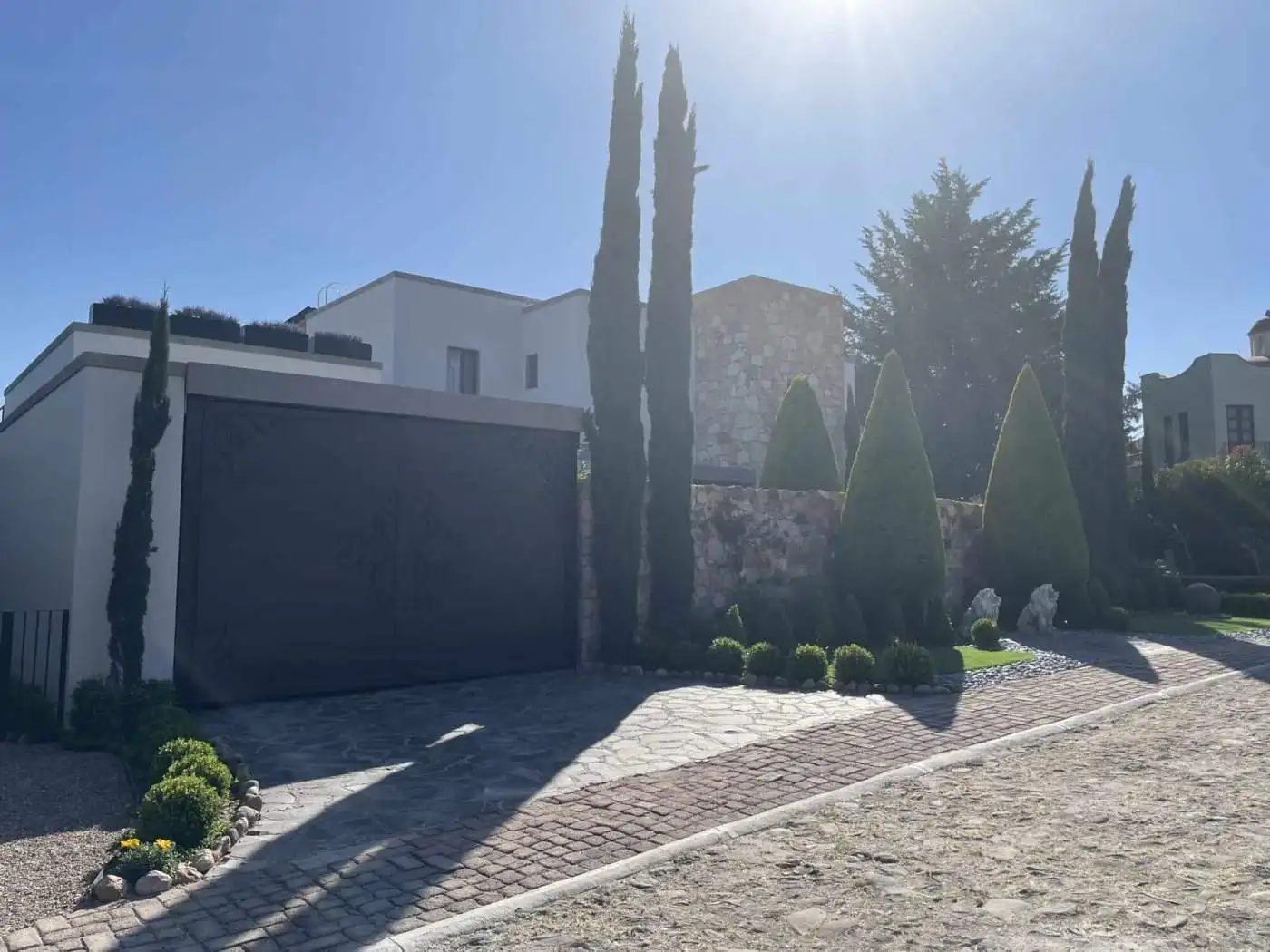 Elegant villa with landscaped garden, tall cypress trees, and modern architecture.