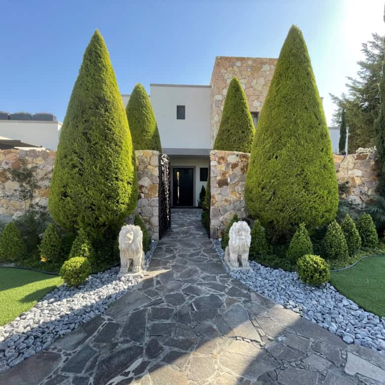 Luxury villa entrance with tall, manicured cypress trees and stone pathway.