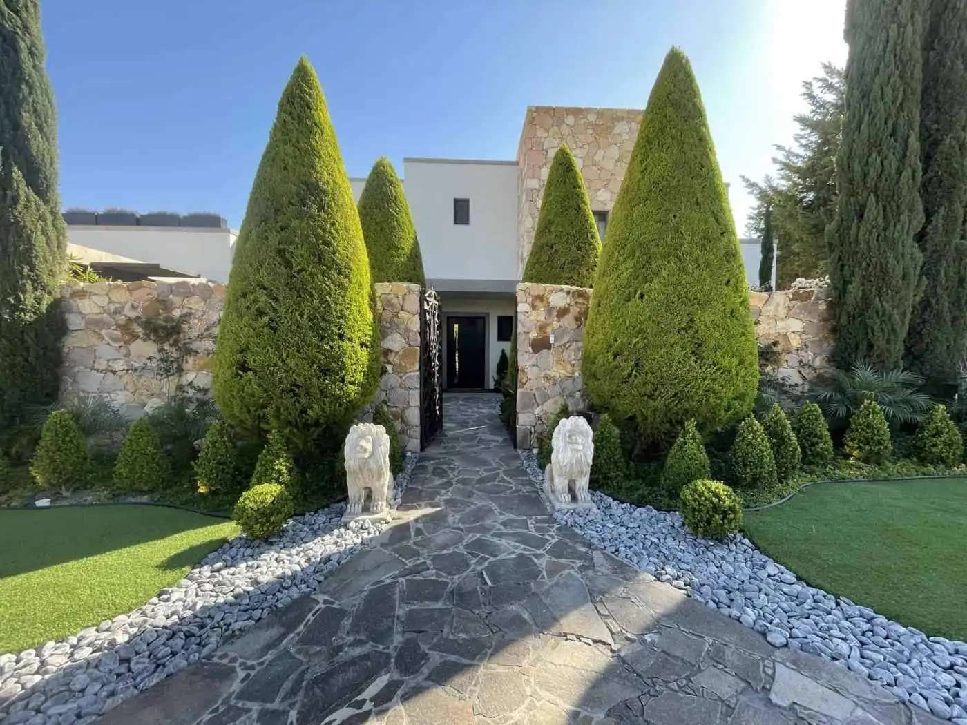 Luxury villa entrance with tall, manicured cypress trees and stone pathway.