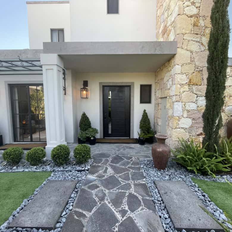 Elegant villa entrance with stone pathway and lush greenery.