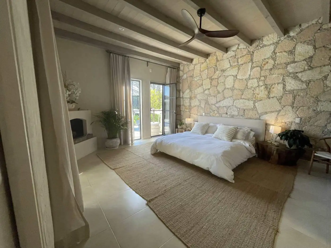 Modern bedroom with stone accent wall, balcony doors, and cozy decor.